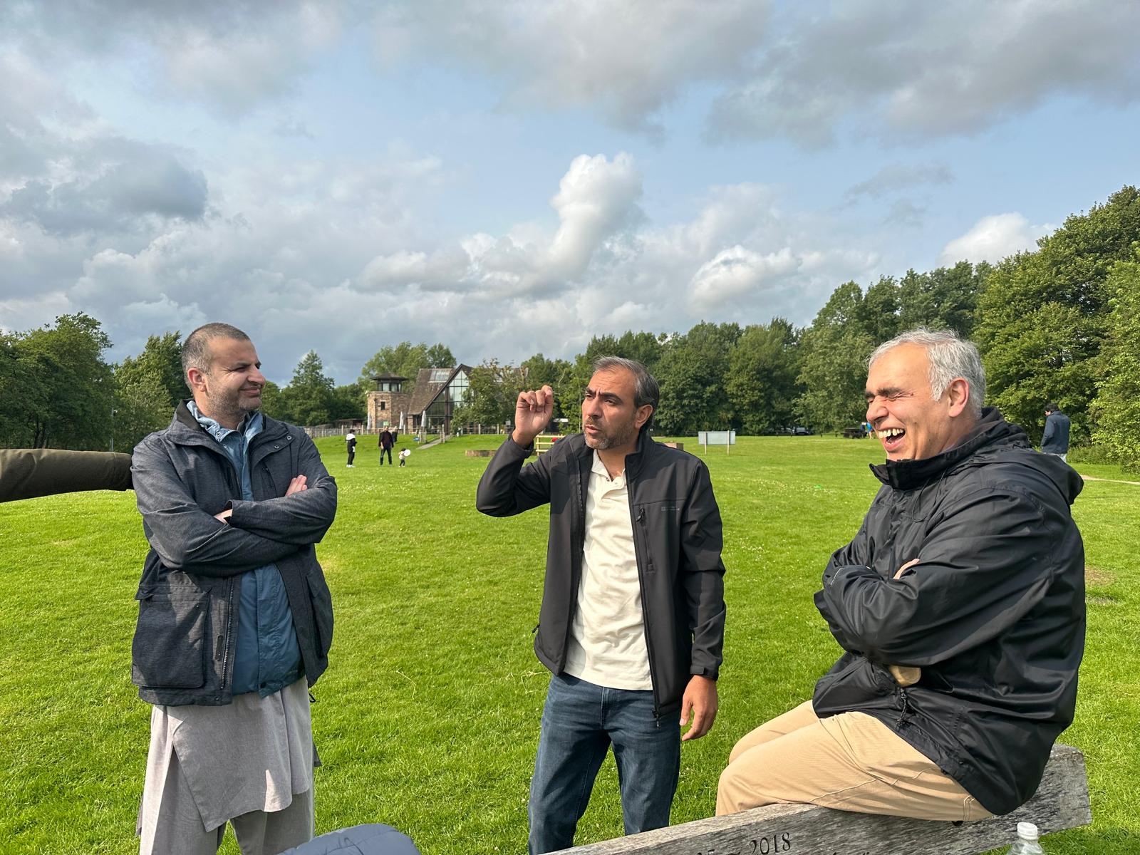 Three of the walkers talking and laughing together in a green field, one of them seated on a bench
