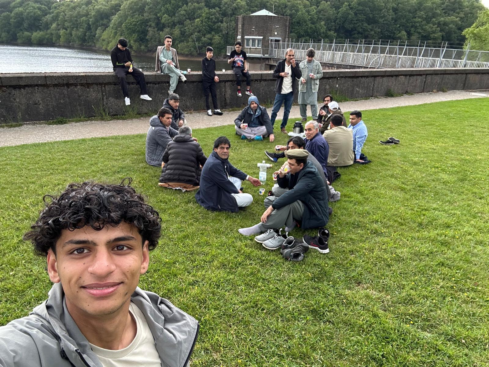 Walkers resting on the grass beside Tittesworth Reservoir with cups of tea in hand, a young man smiling into the camera in the foreground