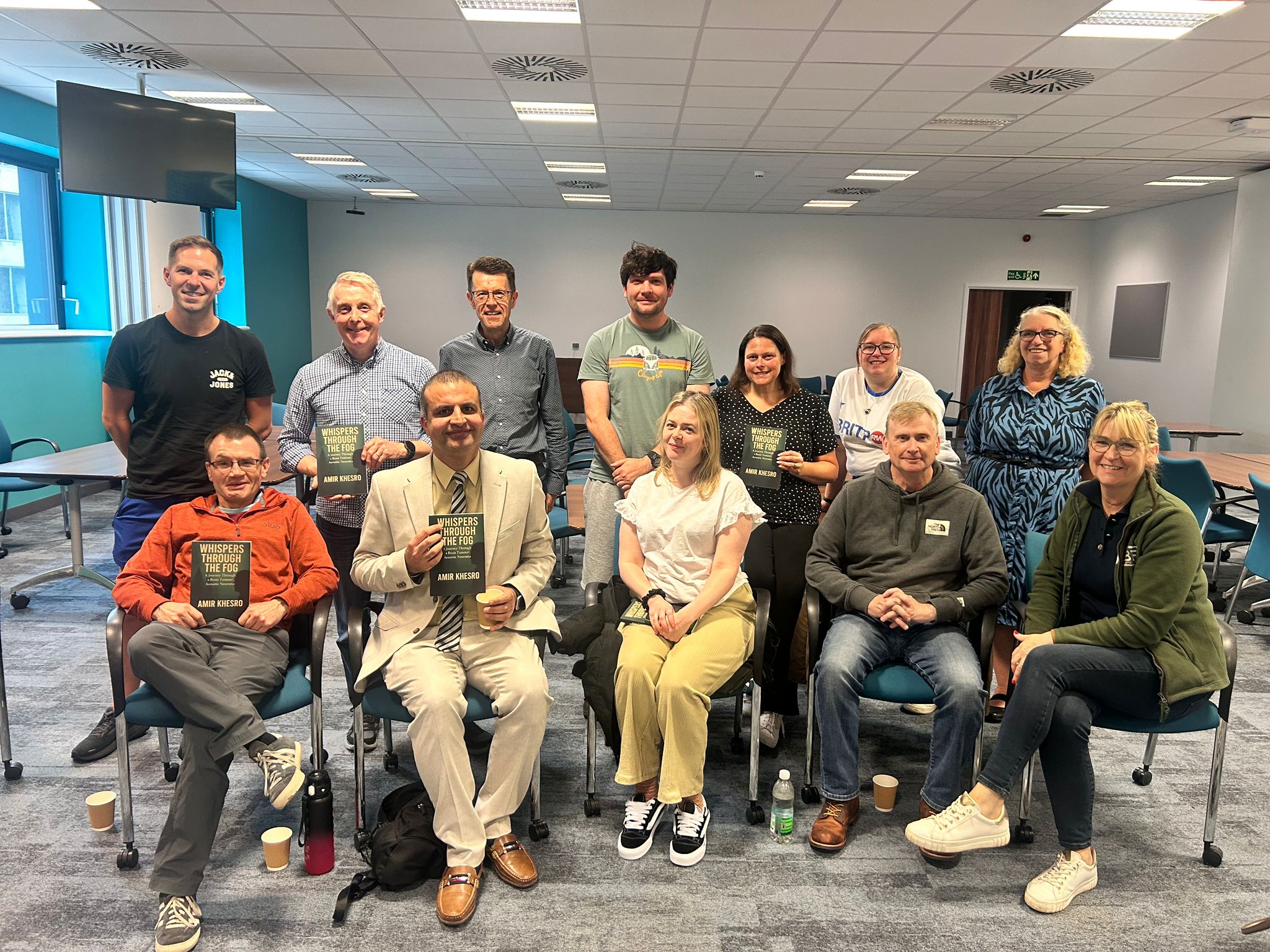 Twelve attendees of the Salford Face-to-Face Meeting gathered for a photograph, several of them holding copies of Whispers Through the Fog